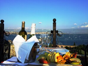 A table with a bottle of wine, glasses, and a fruit platter, overlooking a coastal cityscape. - Mytra Hotel (Istanbul)