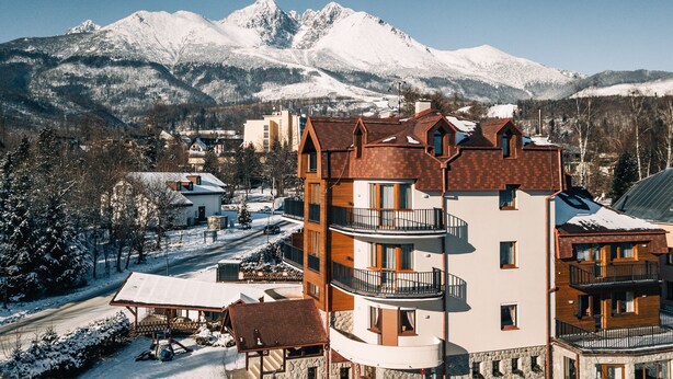 Un hotel de varios pisos con balcones, un paisaje de montaña nevada y cielo despejado.