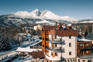 A multi-story hotel with balconies, a snow-covered mountain backdrop, and a clear sky. - APLEND Vila Beatrice (Vysoké Tatry)