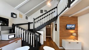 Una cocina moderna con microondas, cafetera y armarios blancos. Una escalera con barandillas negras conduce a otro nivel.