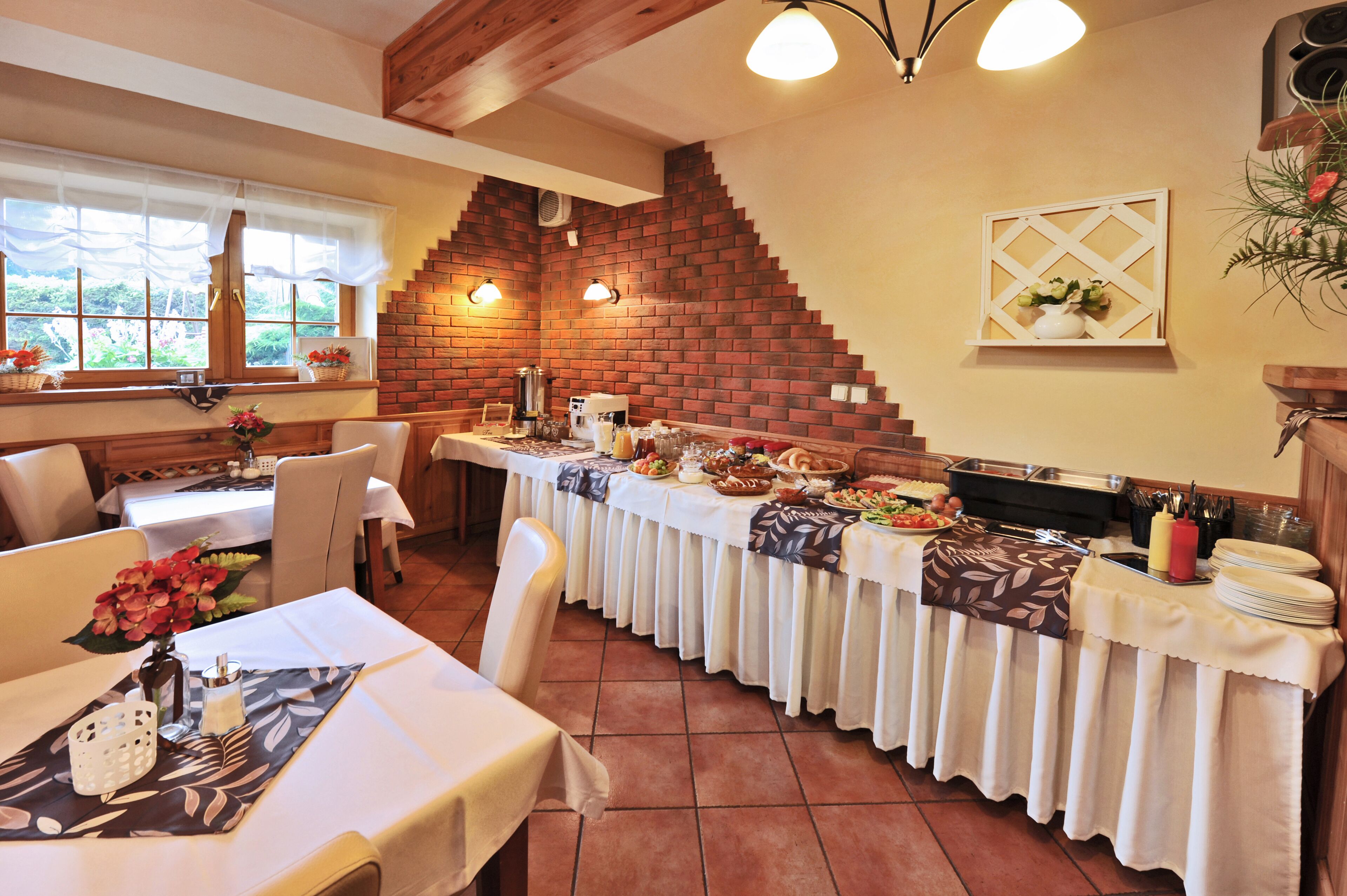 Un comedor con una larga mesa dispuesta para un bufé, una pared de ladrillo y una ventana con cortinas.