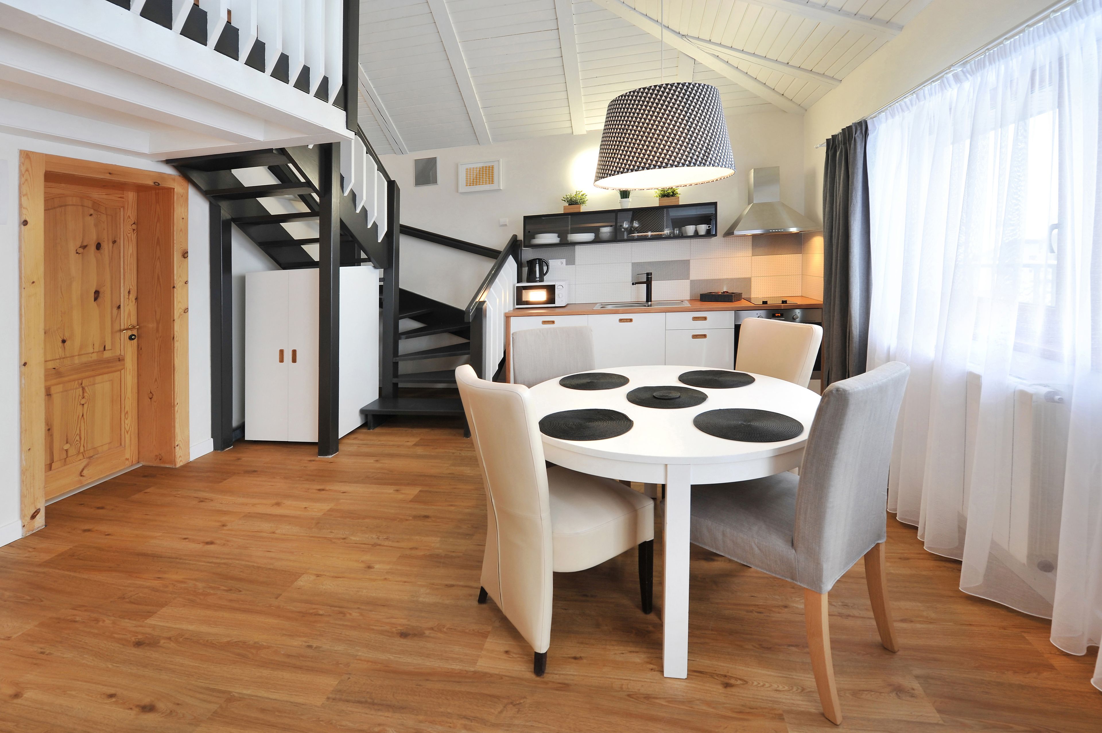A modern kitchen with a central island, a dining area with a round table and chairs, and a staircase leading to an upper level.