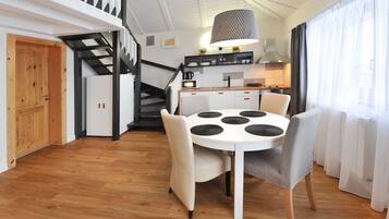 A modern kitchen with a central island, a dining area with a round table and chairs, and a staircase leading to an upper level.