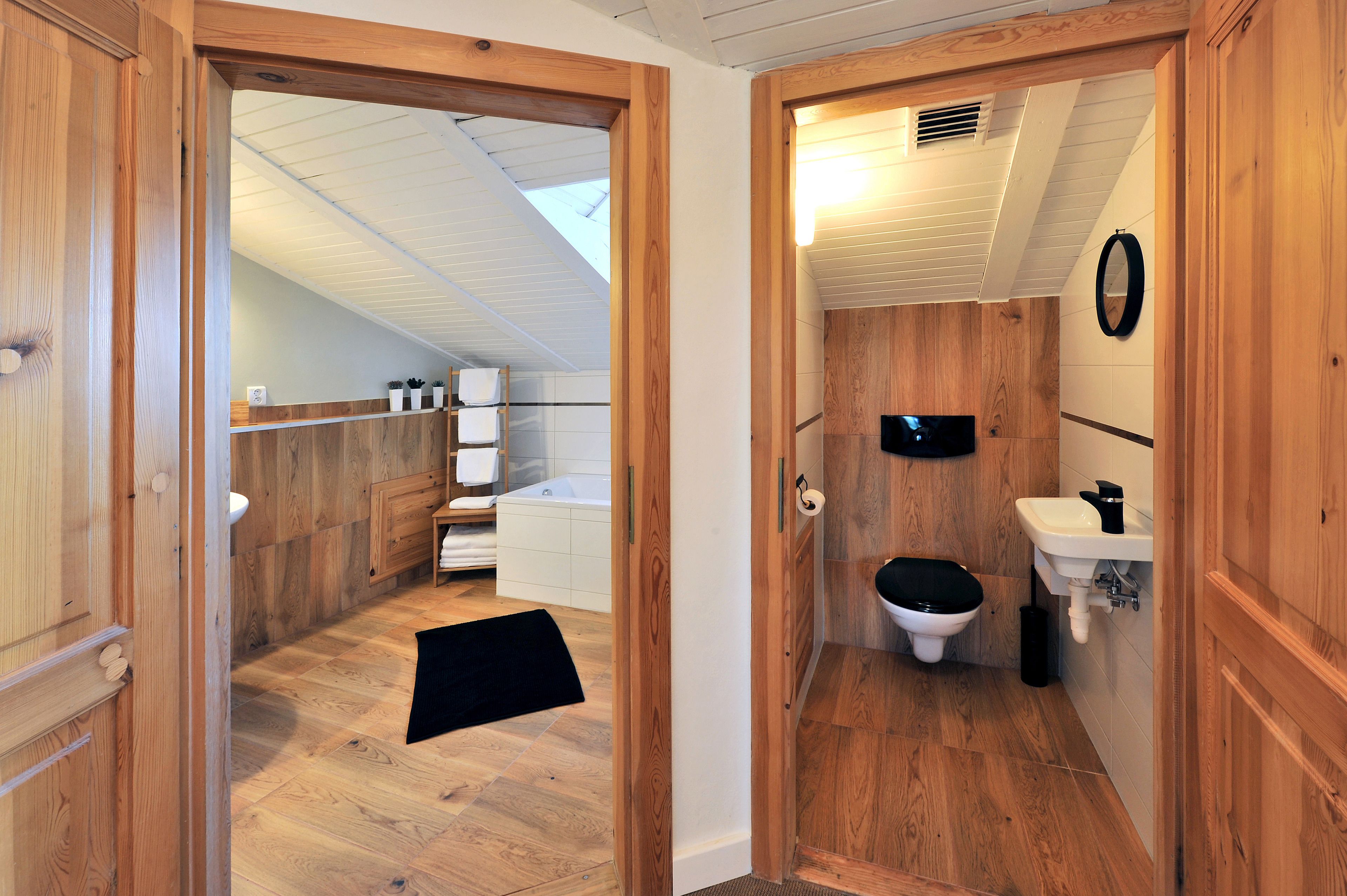 A wooden-floored bathroom with a toilet, sink, and shower area.