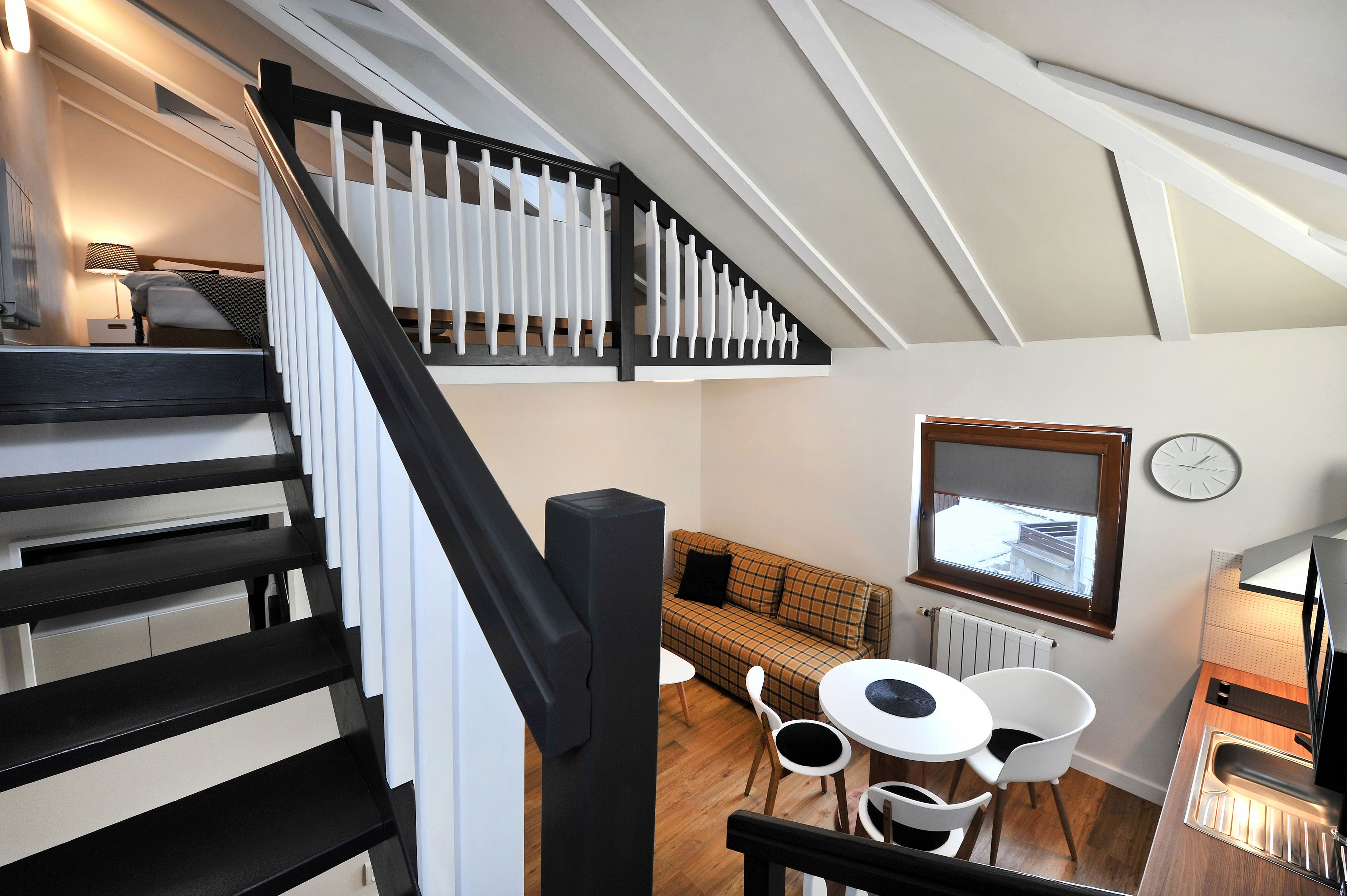 Eine moderne Loft-Wohnung mit Treppe, einem Wohnbereich mit Sofa und Sesseln, einem Esstisch und einer Küchenzeile.
