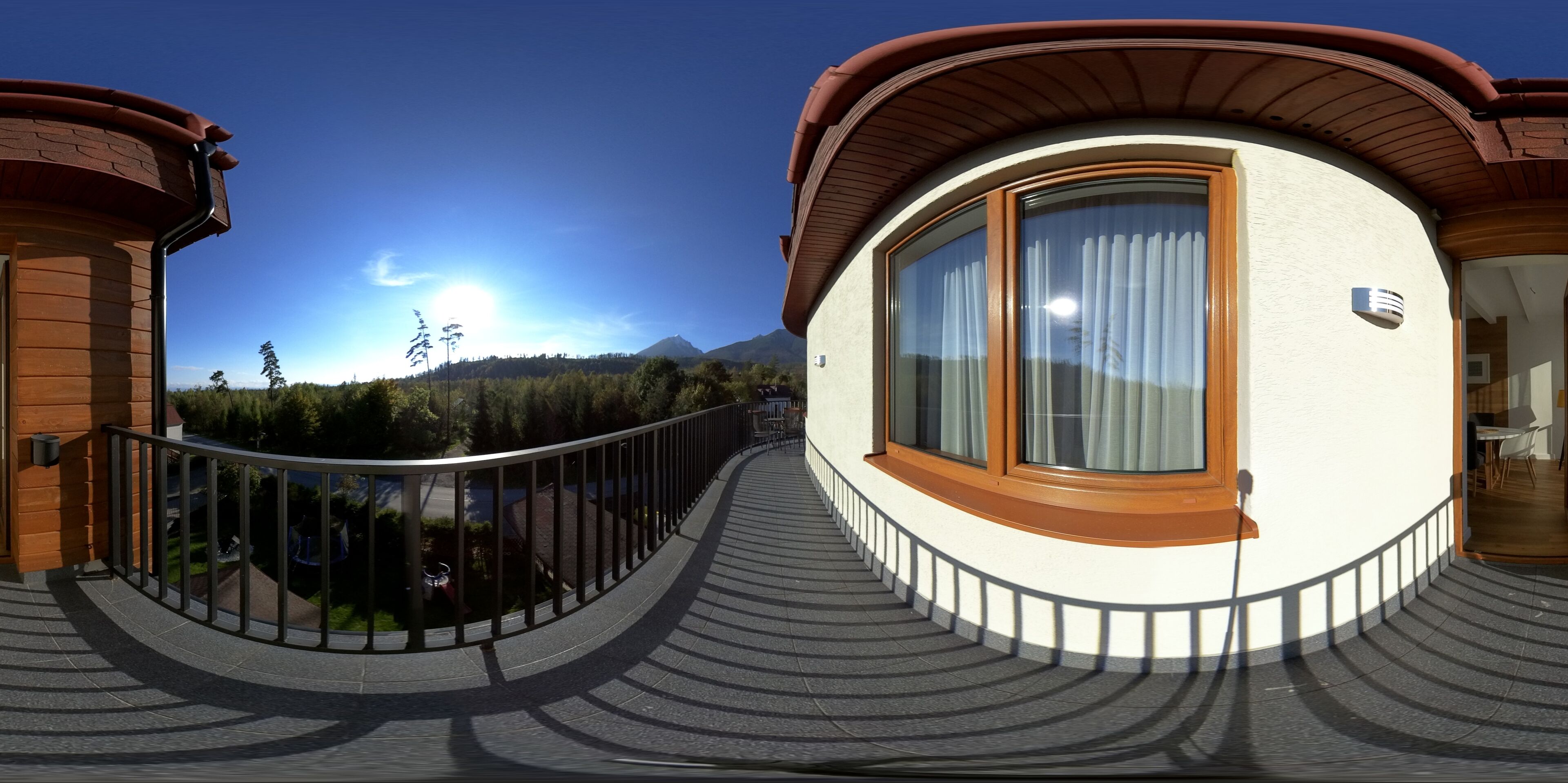 A modern building with a curved balcony, large windows, and a view of a mountain range.