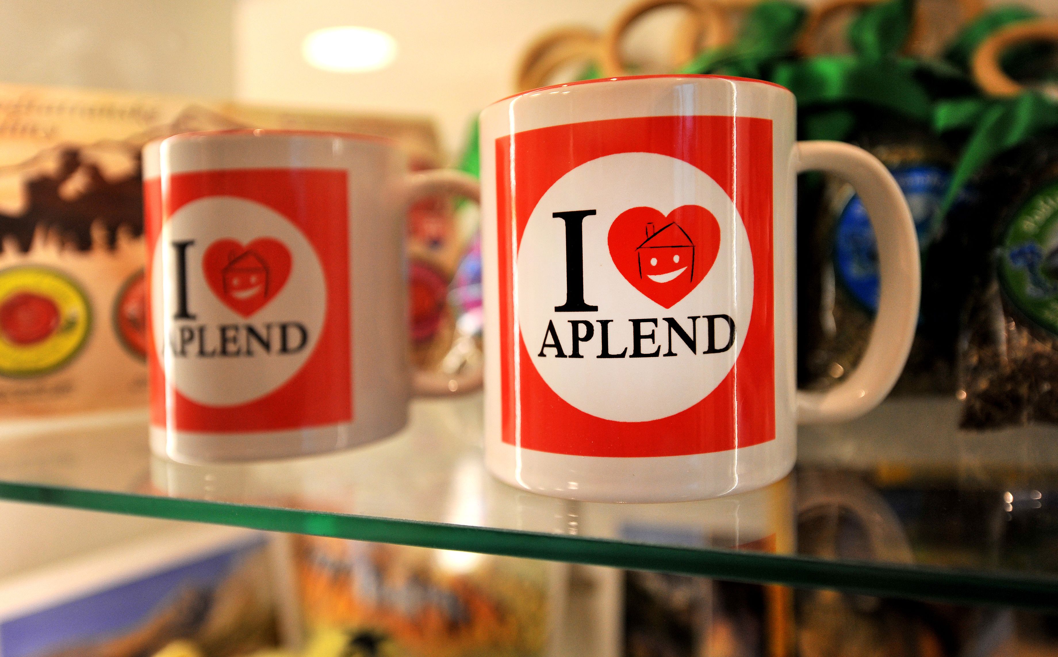Two mugs with 'I ♥ APLEND' printed on them, placed on a glass shelf.