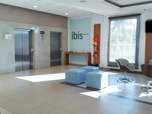 A modern lobby with a reception desk, two elevators, and a seating area with blue ottomans. - Ibis Barretos (Barretos)