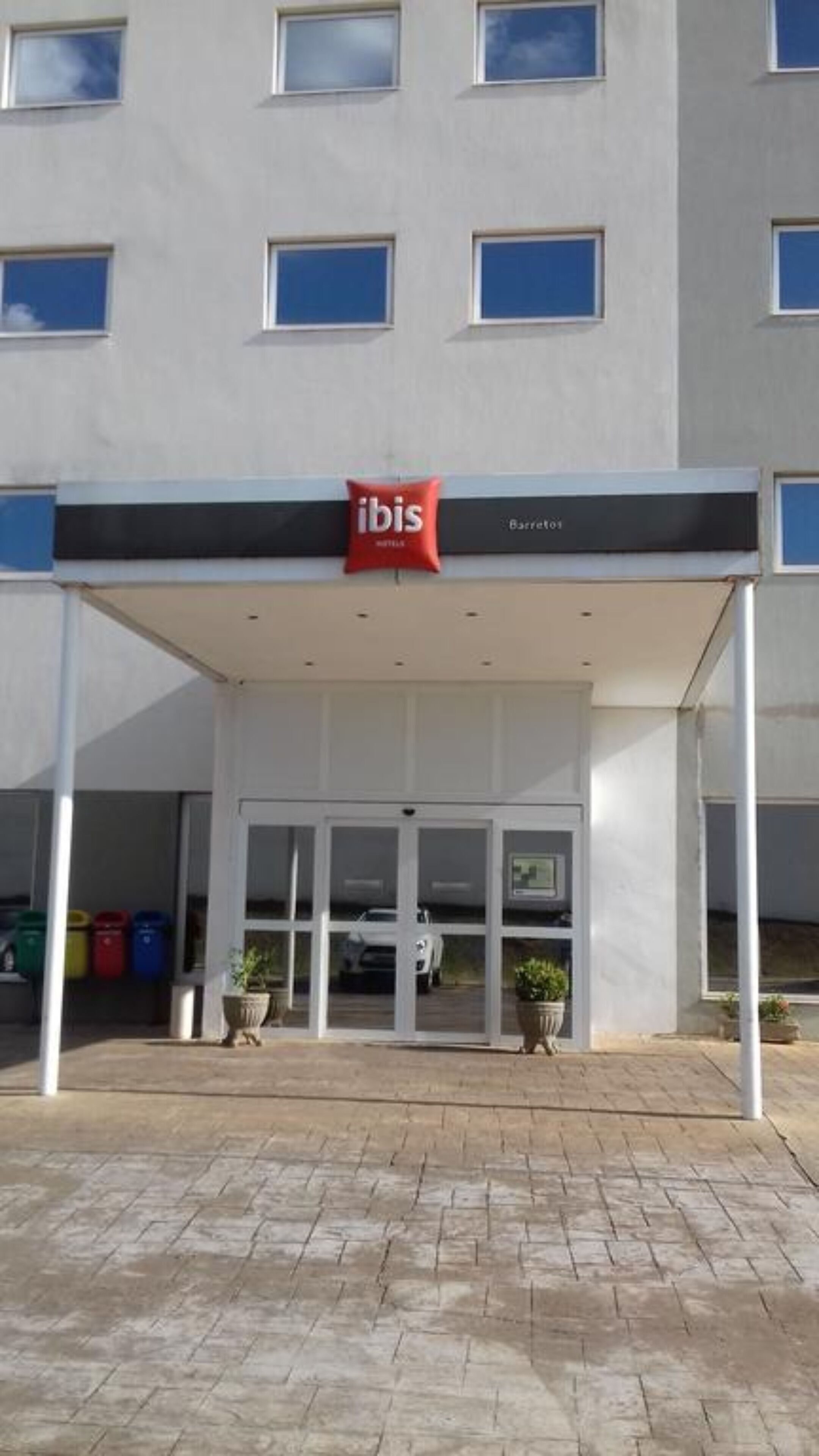 Entrada de un hotel con un área techada, puertas de vidrio y un letrero rojo de 'ibis'.