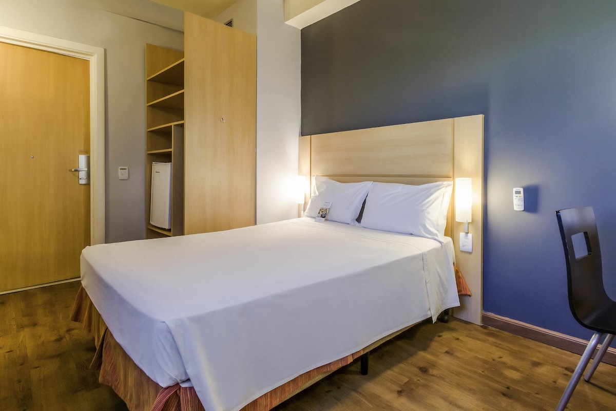 Una habitación de hotel con una cama grande, un armario, un escritorio y una silla.