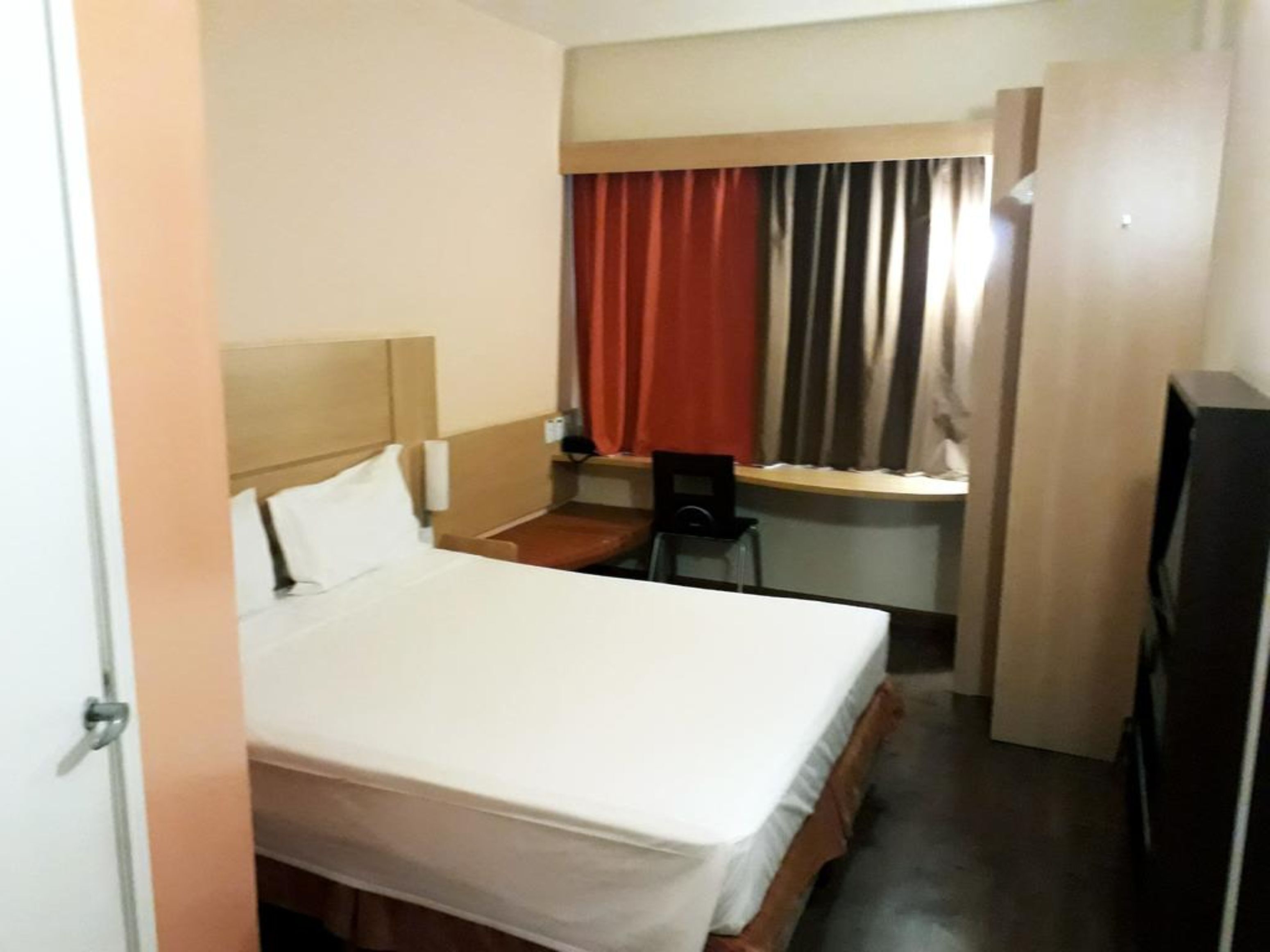 A hotel room with a bed, a desk, a chair, and a television.