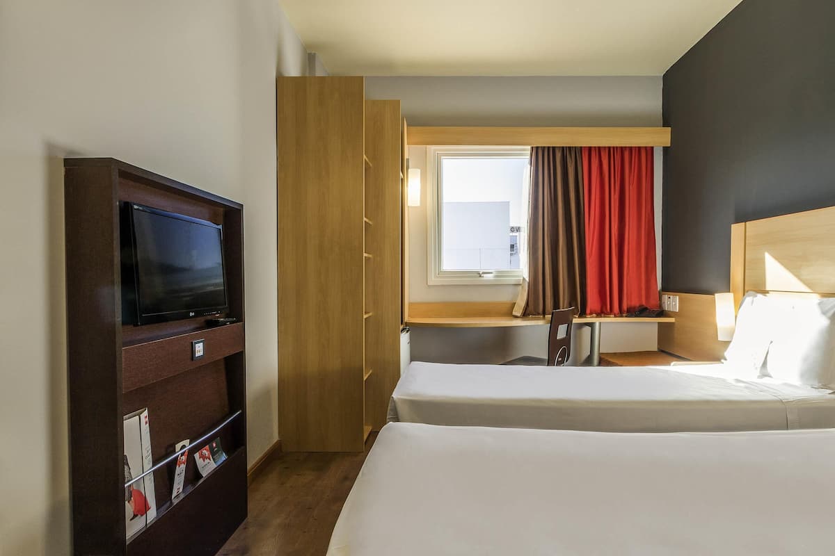 Habitación de hotel con televisión, escritorio, dos camas y ventana con cortinas, con vista al exterior.