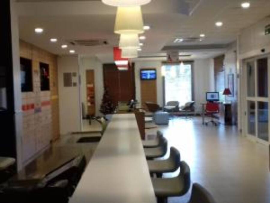 A long dining table with chairs, a whiteboard, and a television screen in a well-lit room with large windows.