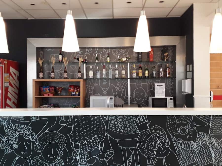 A bar area with a black and white mural, shelves with bottles, snacks, and a microwave.