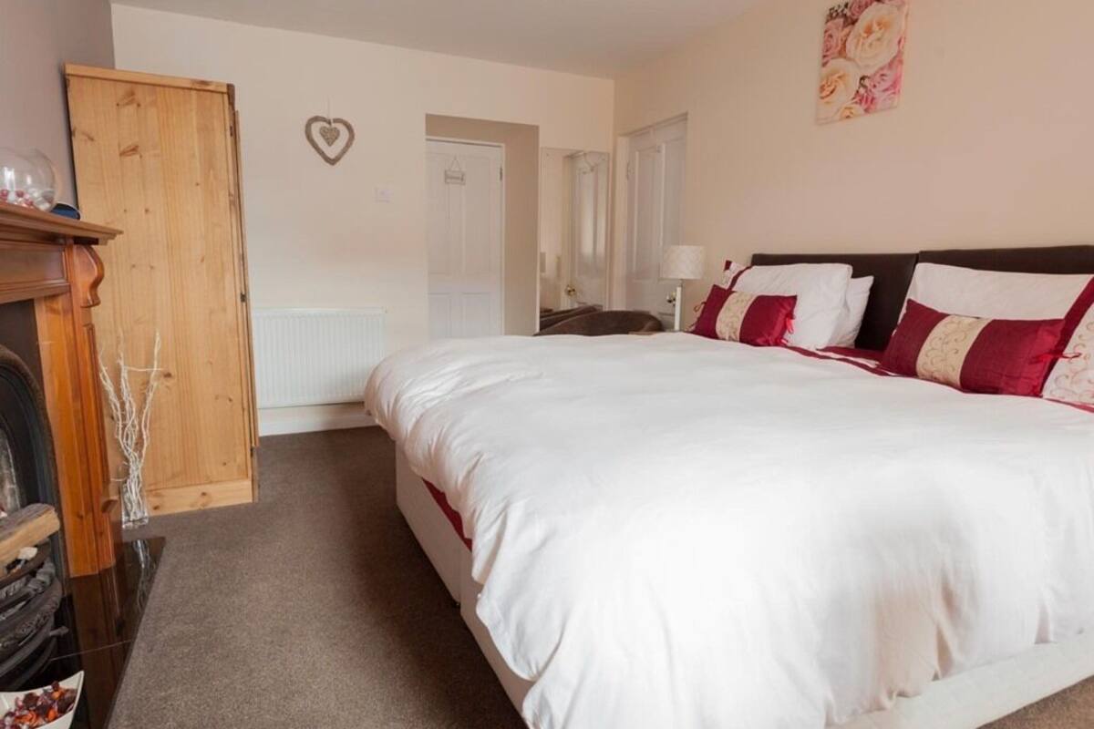 A bedroom with a large bed, a wooden wardrobe, a radiator, and a heart-shaped decoration on the wall.