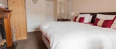 A bedroom with a large bed, a wooden wardrobe, a radiator, and a heart-shaped decoration on the wall.