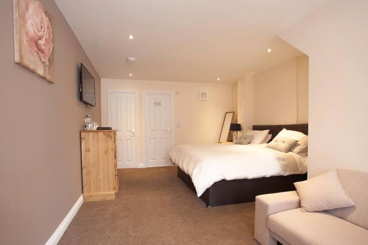 A bedroom with a bed, a wooden cabinet, a television, and a couch.