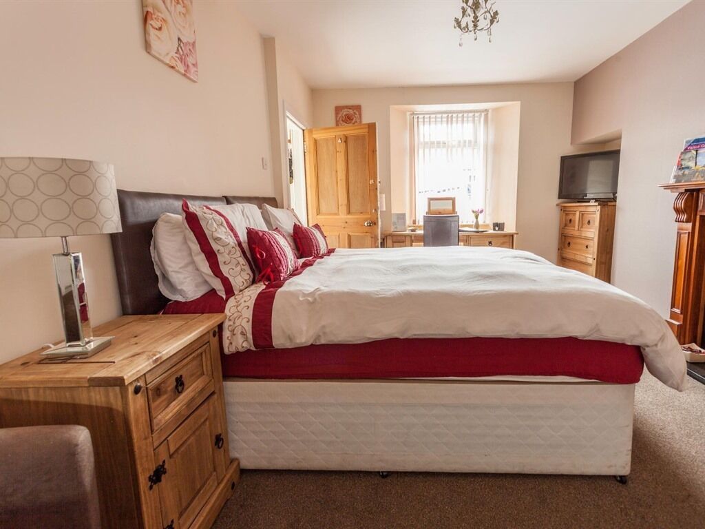 A bedroom with a bed, wooden nightstand, dresser, and a television on a stand.