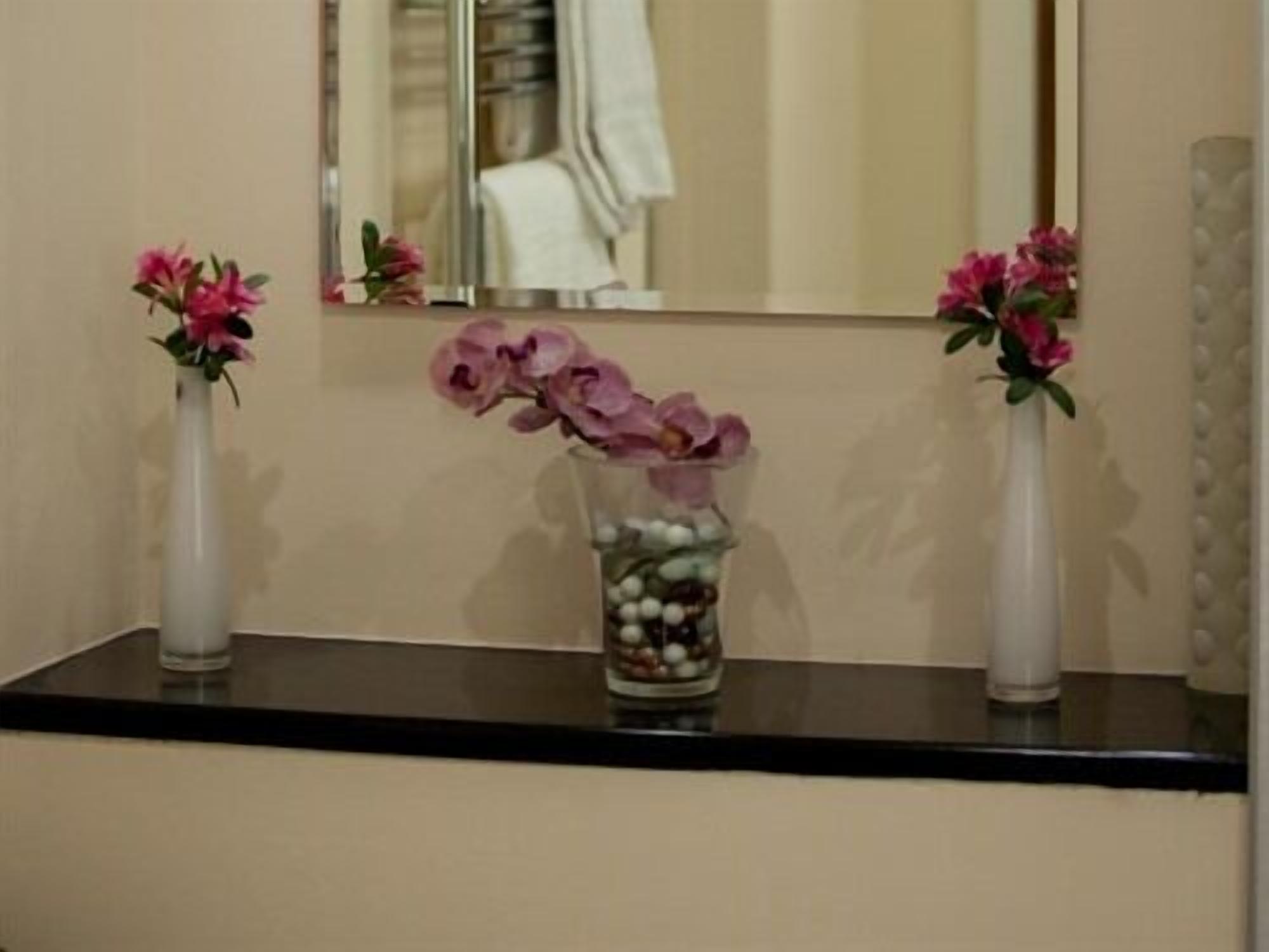 A bathroom vanity with two white vases containing pink flowers, one with a larger vase filled with white pebbles and pink flowers, and a mirror above.