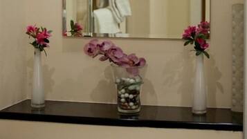 A bathroom vanity with two white vases containing pink flowers, one with a larger vase filled with white pebbles and pink flowers, and a mirror above.