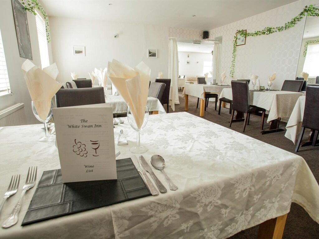 A dining area at The White Swan Inn with tables set for a meal, a wine list sign, and a view of the adjacent room.