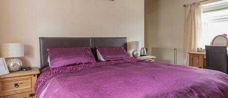 A bedroom with a large bed, wooden nightstands, a dresser, and a window with curtains.