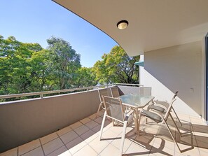 A balcony with a glass table and chairs, a white railing, and a view of trees. - Inn on the Park Apartments (Toowong)