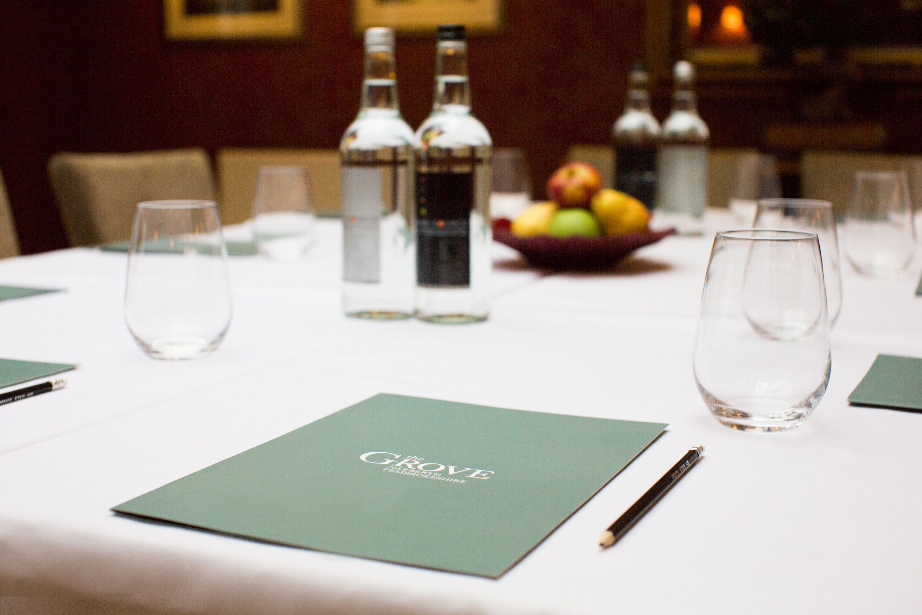 A dining table set with a menu, glasses, and bottles of water.