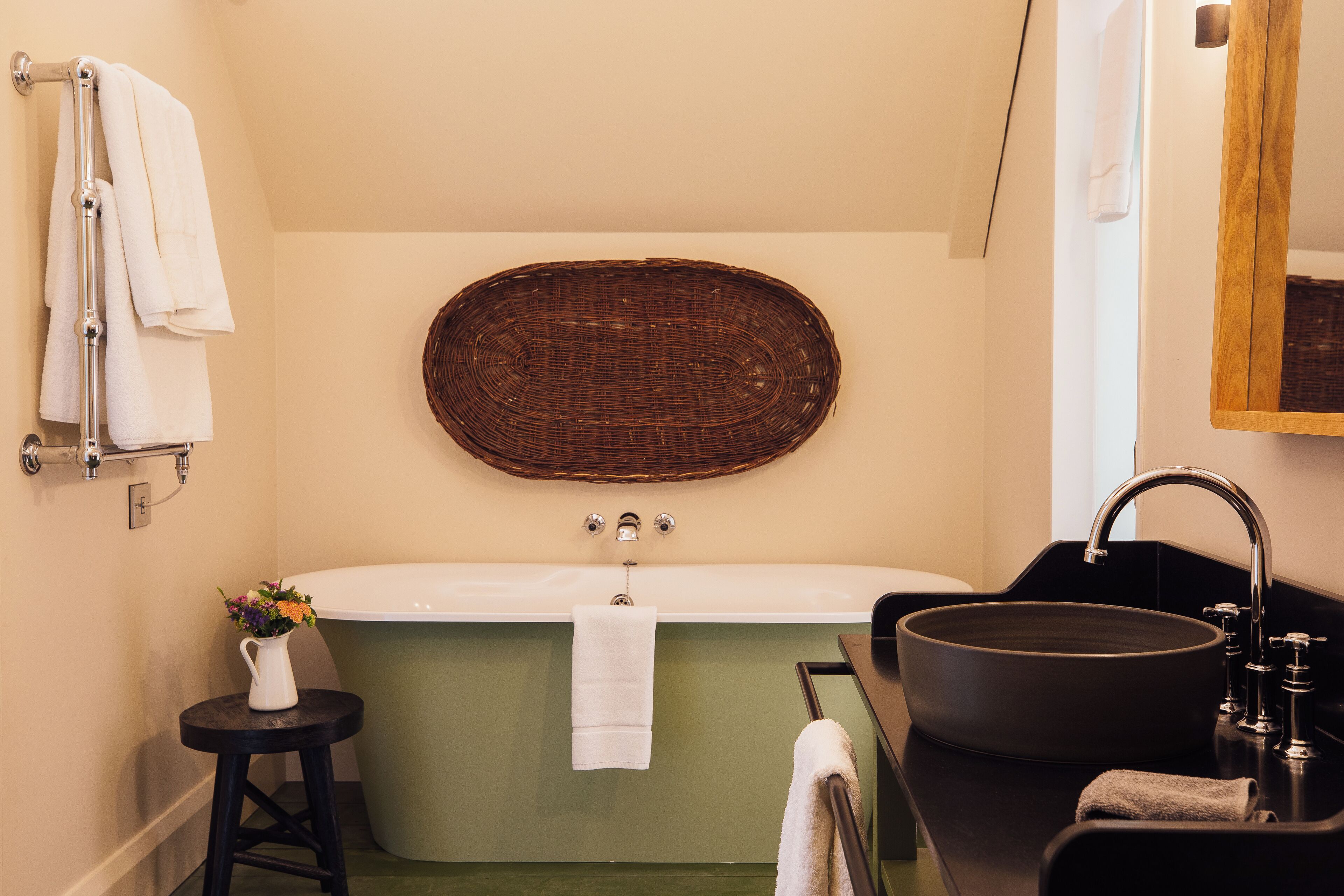 Un bagno con una vasca freestanding, un lavandino nero e una decorazione murale in vimini.