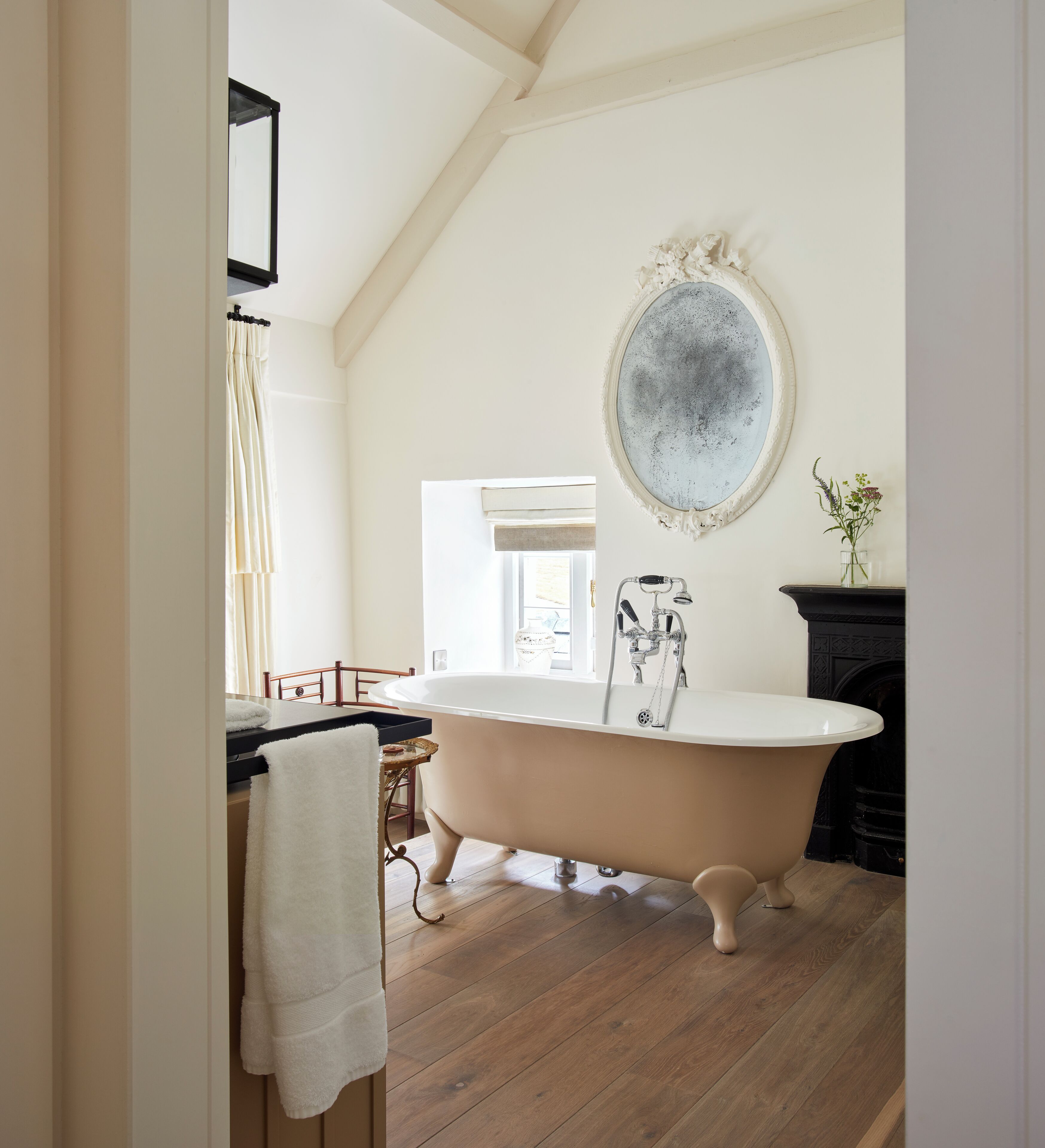 A bathroom with a freestanding bathtub, a mirror, and a wooden floor.