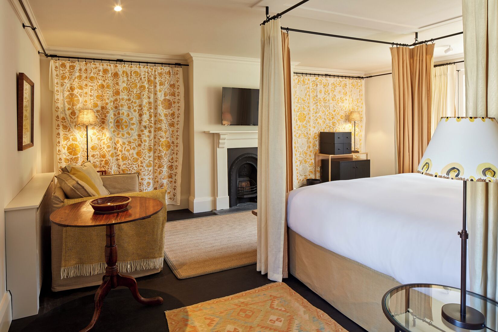 Una habitación de hotel con cama, sofá, una mesita, chimenea y televisión.