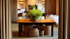 Un comedor con una mesa central decorada con una gran planta en maceta, rodeada de cestas de mimbre y mesas dispuestas.