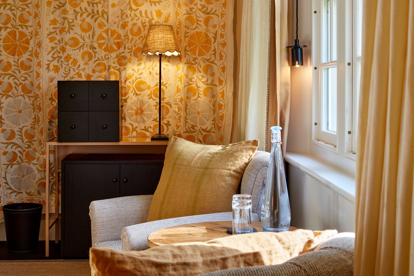 A cozy room with a patterned wallpaper, a lamp, a bottle, and a small table.