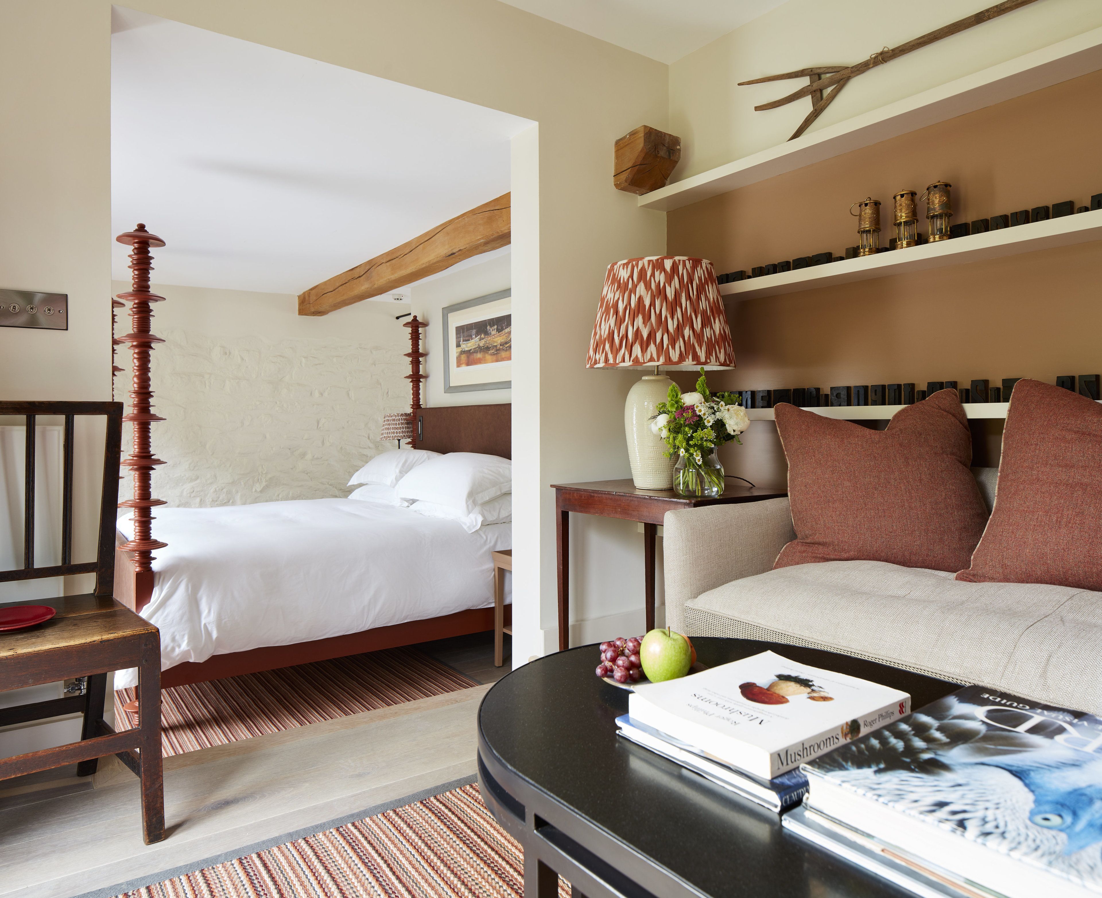 Une chambre d’hôtel avec un lit, un canapé, une table avec un livre et des fruits, et une lampe.