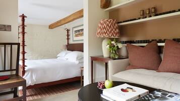 A hotel room with a bed, a sofa, a table with a book and fruit, and a lamp.