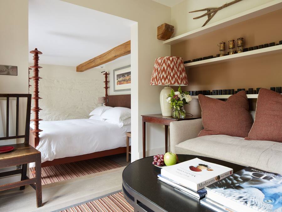 A hotel room with a bed, a sofa, a table with a book and fruit, and a lamp.