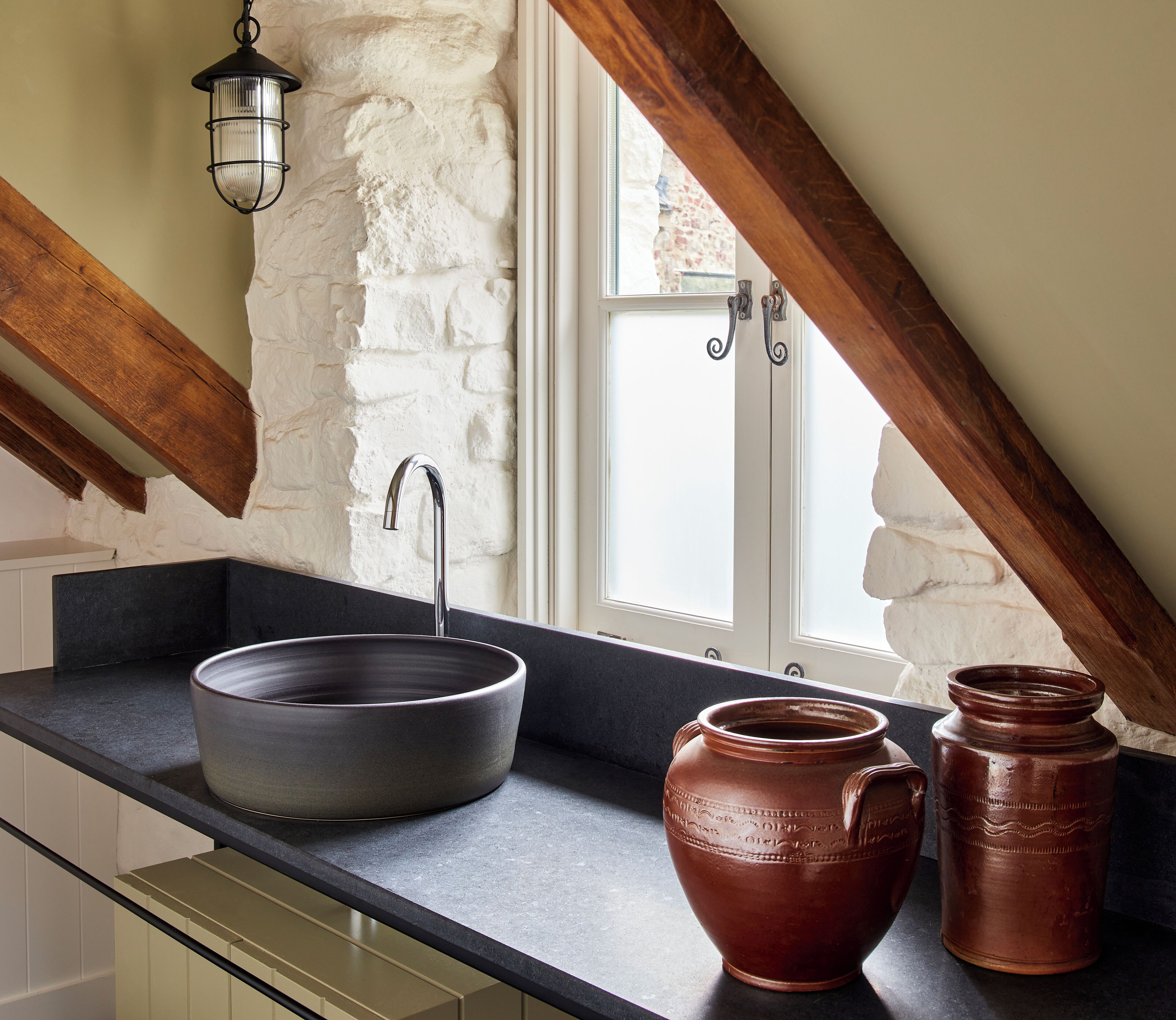 A kitchen with a stone wall, a window, and a black countertop.