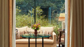A cozy room with a glass table, a beige sofa, and a view of a garden through a large window.