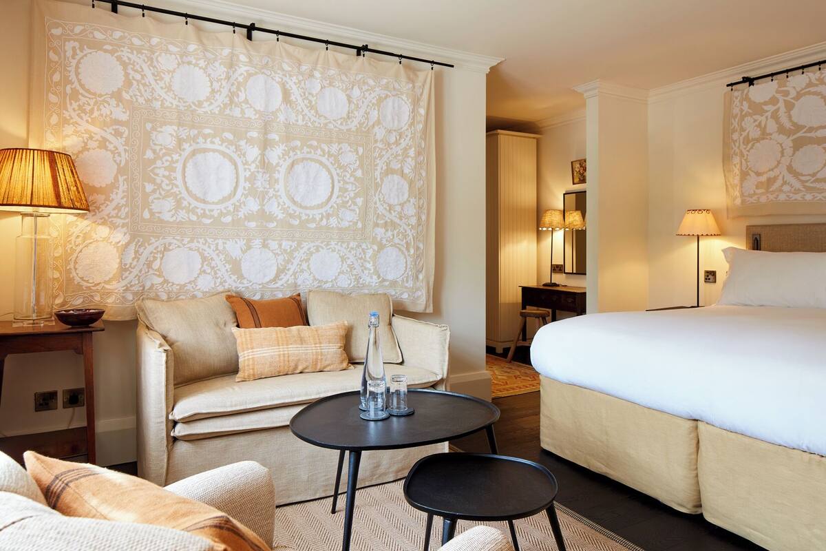 A hotel room with a bed, a sofa, a small table, and a lamp.