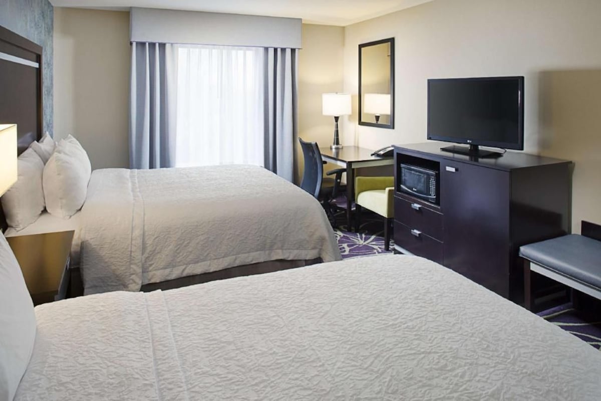 A hotel room with two beds, a desk with a TV, a microwave, and a chair.