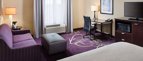 Habitación de hotel con cama, escritorio, silla, televisor, microondas y ventana con cortinas.