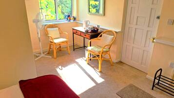 A room with a bed, two chairs, a desk, a window with a view of trees, and a door.