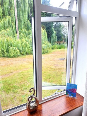 A window with a view of a grassy yard and trees. - Bartles Lodge (Dereham)