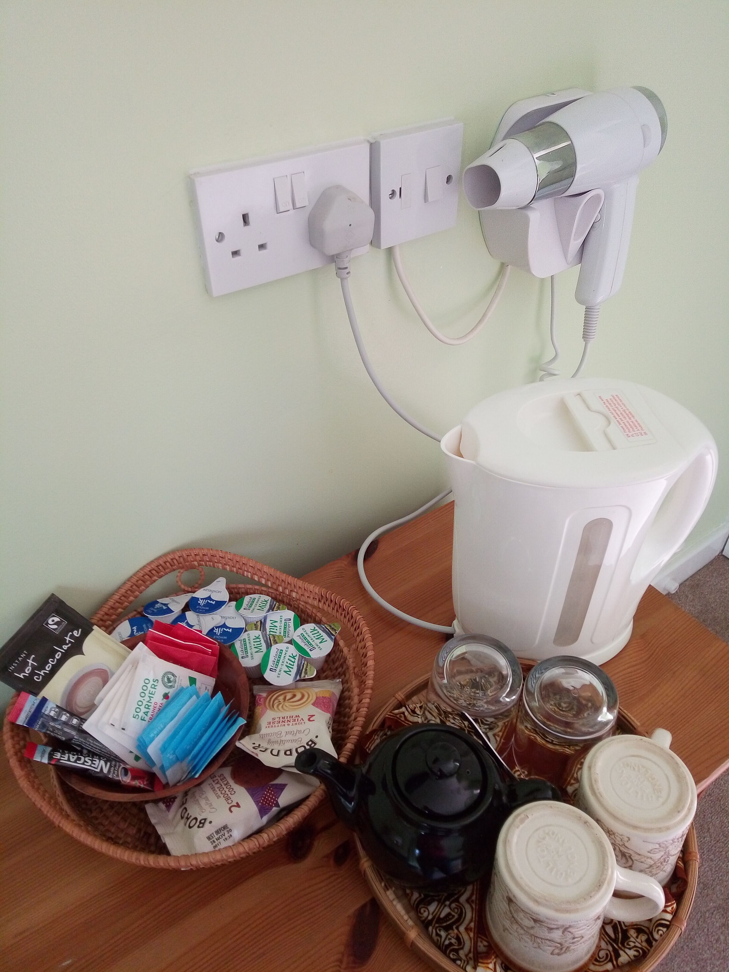 Ein Tisch mit einer Snack-Korb, einem Wasserkocher, einer Teekanne und einem an die Steckdose angeschlossenen Föhn.