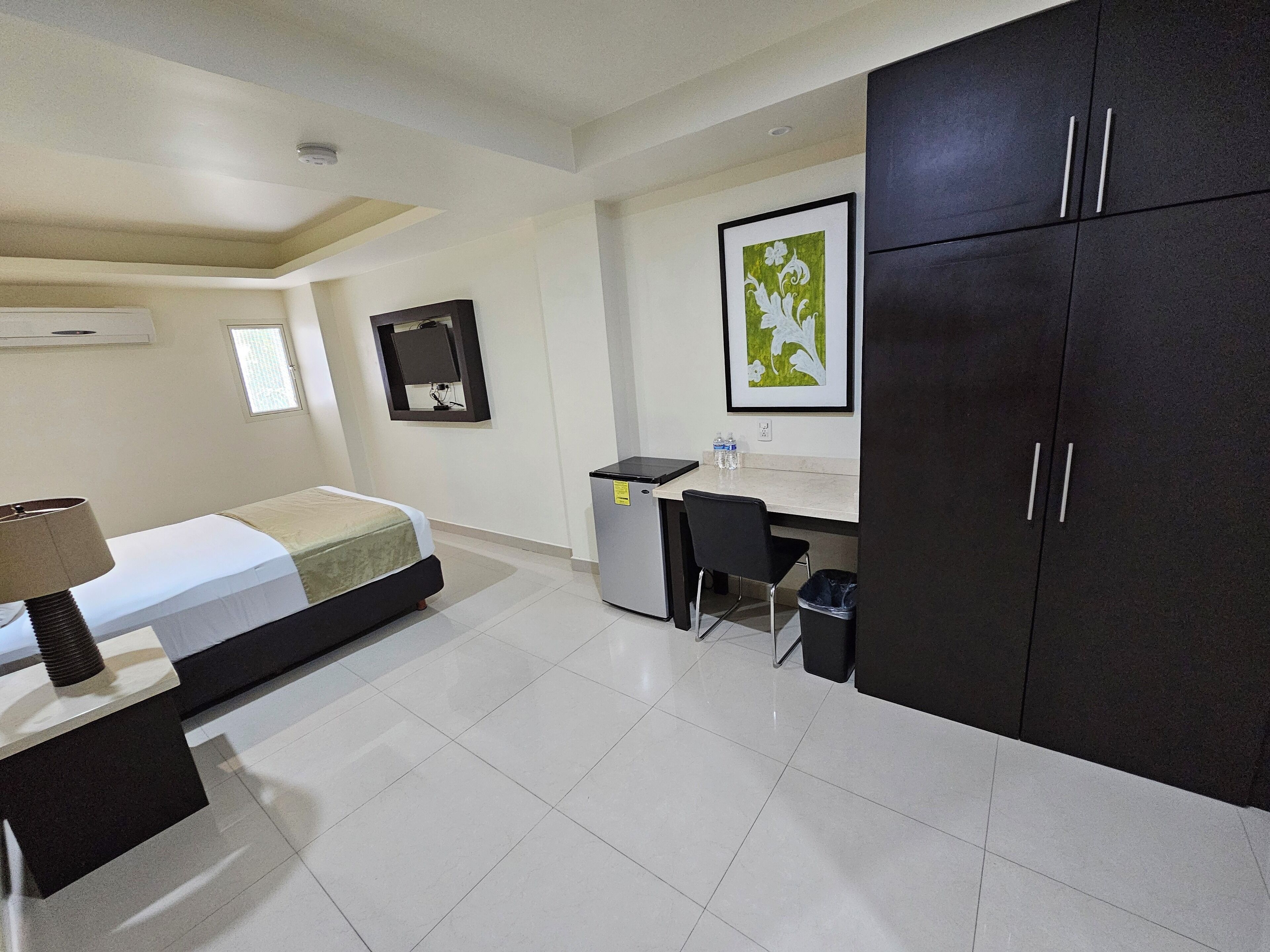 Quarto de hotel com cama, escrivaninha, cadeira e guarda-roupa.
