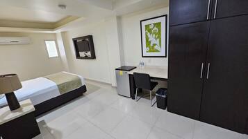Quarto de hotel com cama, escrivaninha, cadeira e guarda-roupa.
