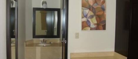 A small, modern room with a bed, a desk with a chair, a mirror, and a wall-mounted air conditioner.
