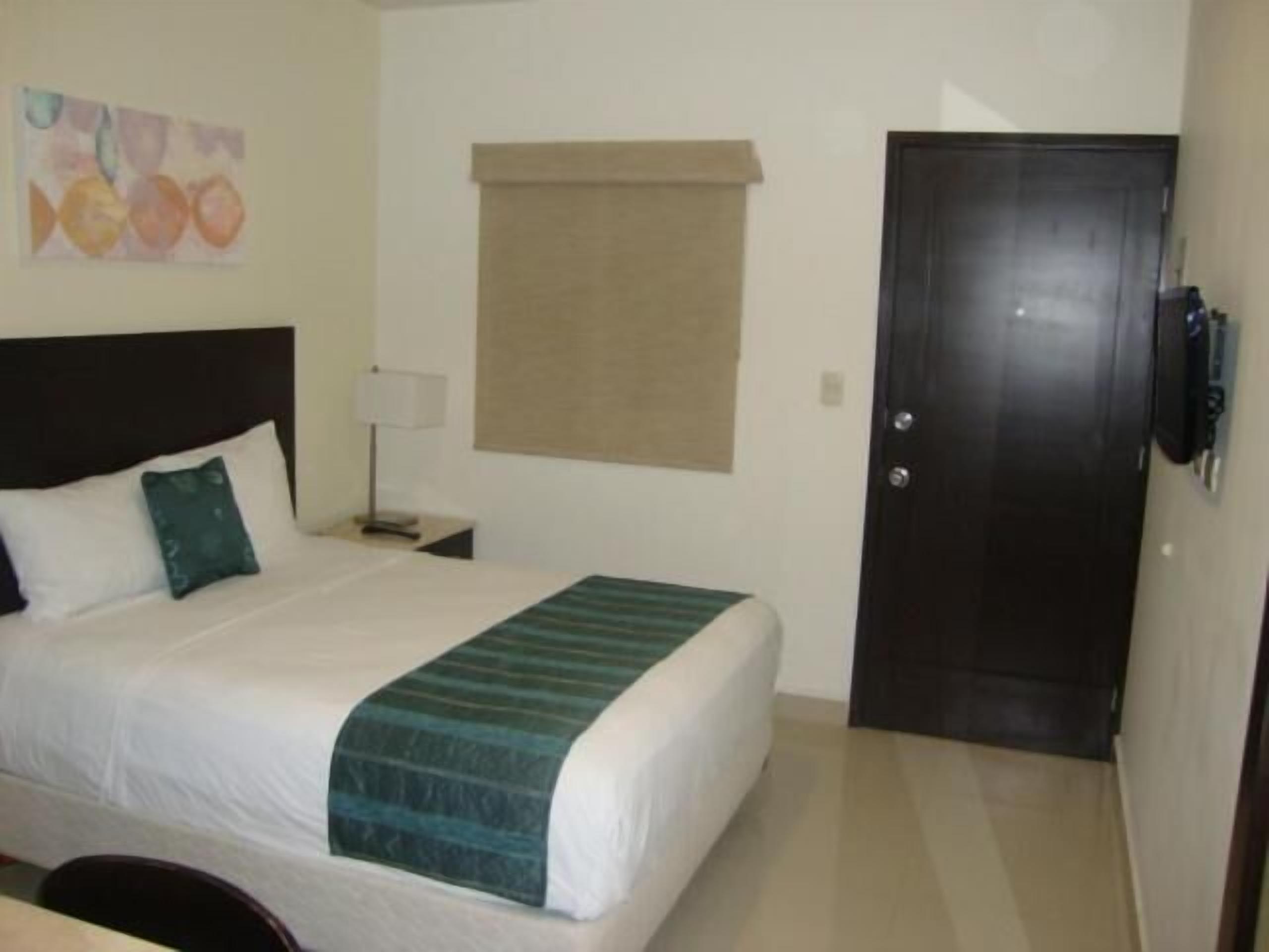 Une chambre d’hôtel avec un lit, une table de chevet, une lampe, une porte et un téléviseur fixé au mur.