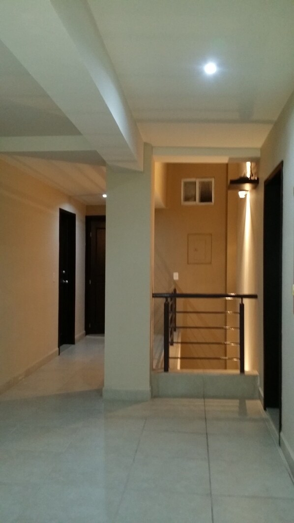 A spacious hallway with a staircase leading to an upper floor. The walls are plain, and the floor is tiled.