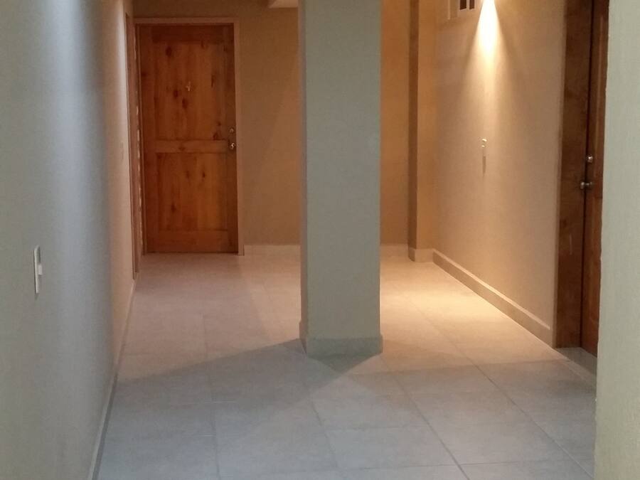 A hallway with tiled flooring, a wooden door at the end, and a pillar with a light fixture.